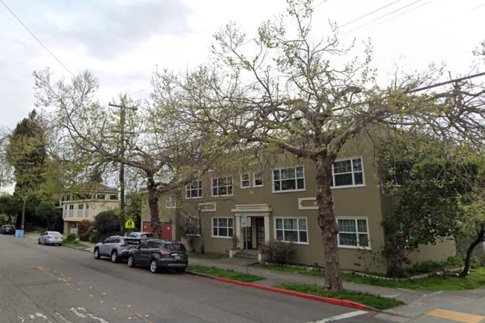 Two-story green apartment building in residential neighborhood in Berkeley, California with tall street trees.